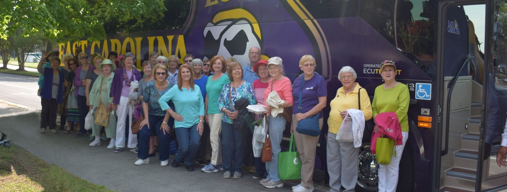 Group of Lifelong Learning Program participants in front of an ECU bus on a trip